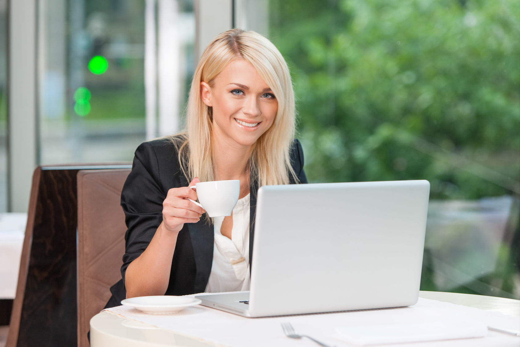 Blond business lady smiling at camera while sitting and drinking coffee or tea.